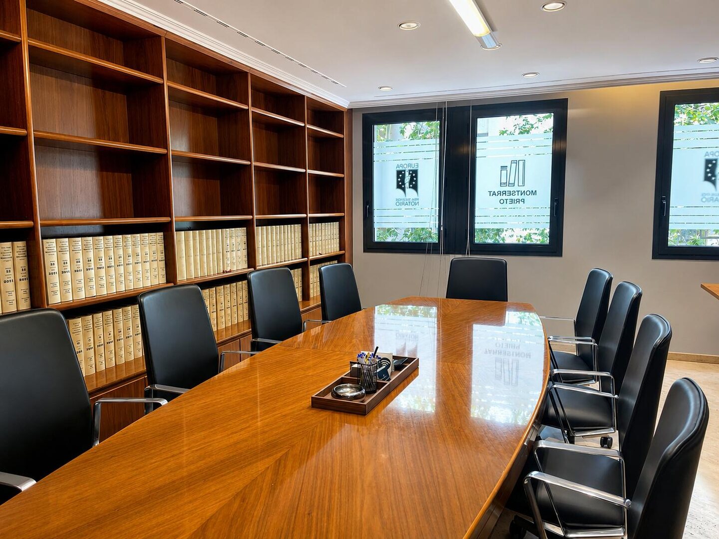 Sala de reuniones con mesa ovalada de madera y biblioteca jurídica